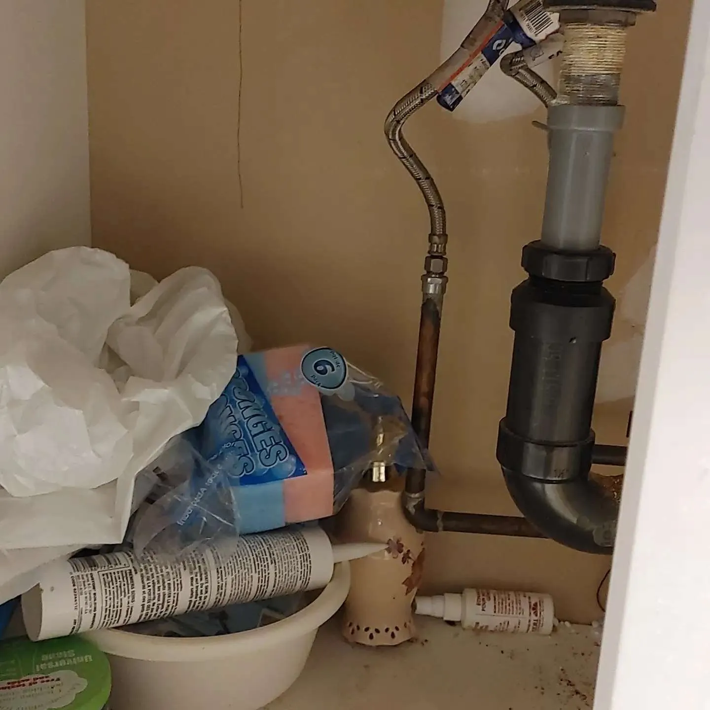 Burst pipe and water leak under sink cabinet with visible water damage and corroded plumbing connections